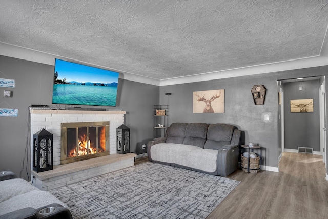 living room featuring visible vents, a brick fireplace, wood finished floors, baseboards, and a textured ceiling