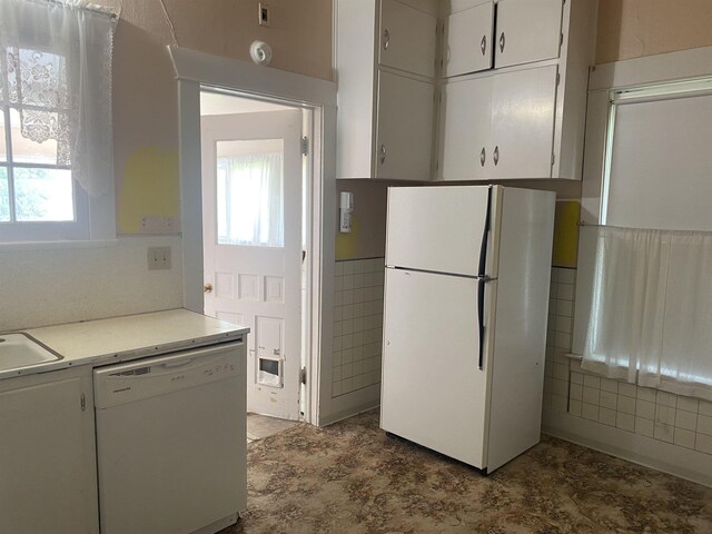 kitchen with white appliances, tile walls, light countertops, a wainscoted wall, and white cabinets