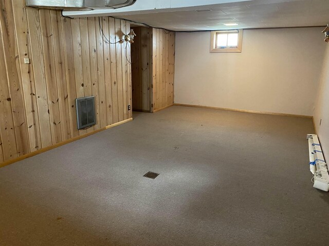 below grade area featuring wooden walls, baseboards, heating unit, and carpet
