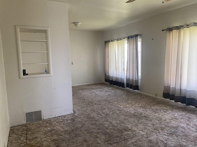 carpeted spare room with baseboards, ceiling fan, and visible vents