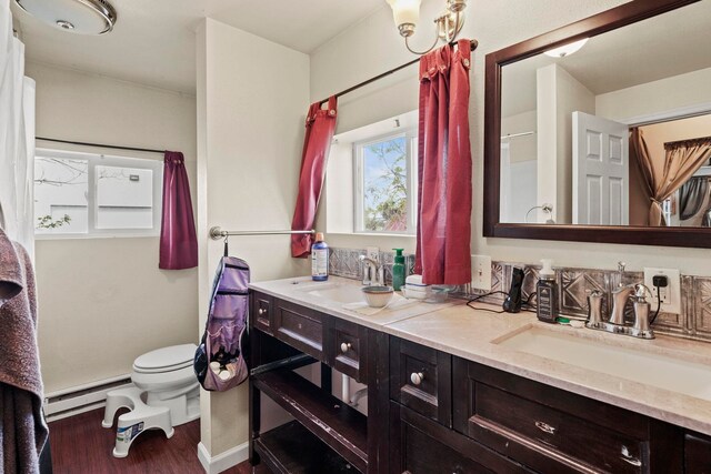 full bath featuring a sink, toilet, double vanity, wood finished floors, and a baseboard radiator