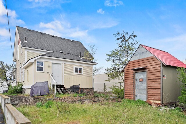 back of property featuring an outbuilding, a shingled roof, and entry steps