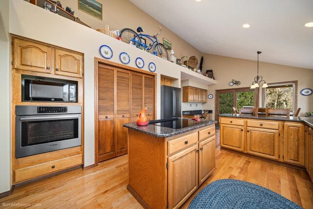 kitchen with lofted ceiling, a center island, light wood finished floors, black appliances, and decorative light fixtures