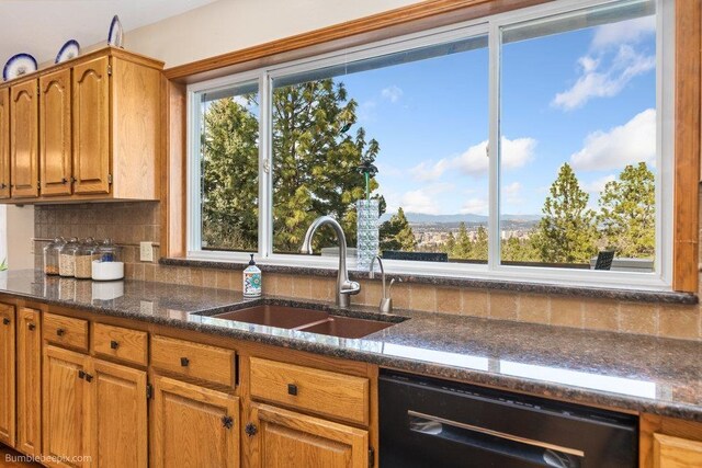 kitchen featuring brown cabinetry, tasteful backsplash, a sink, dark stone countertops, and dishwasher