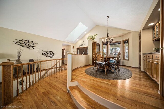 dining room featuring high vaulted ceiling, wood finished floors, a notable chandelier, and a skylight