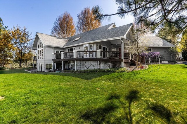 rear view of property featuring roof with shingles, a wooden deck, and a yard