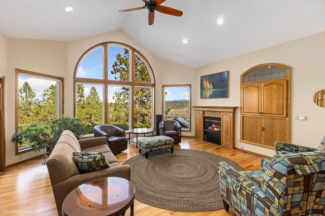 living area featuring ceiling fan, high vaulted ceiling, light wood finished floors, a warm lit fireplace, and recessed lighting