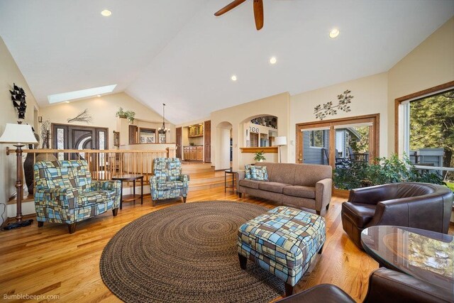 living area featuring arched walkways, light wood-style flooring, a ceiling fan, recessed lighting, and a skylight