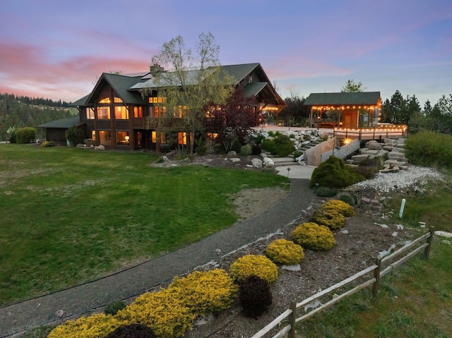 back of house at dusk with a lawn and fence
