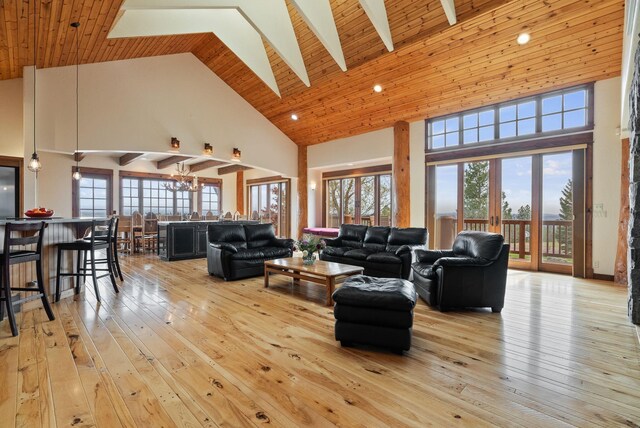 living area featuring beam ceiling, high vaulted ceiling, light wood-type flooring, a chandelier, and wooden ceiling