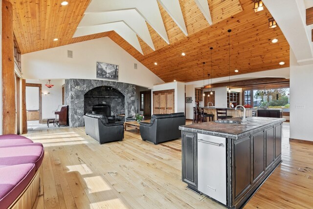 kitchen featuring dark countertops, open floor plan, high vaulted ceiling, light wood-type flooring, and a sink