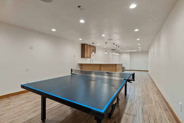 recreation room featuring recessed lighting, baseboards, indoor wet bar, and light wood finished floors