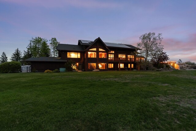 back of house at dusk featuring a lawn, solar panels, and a wooden deck