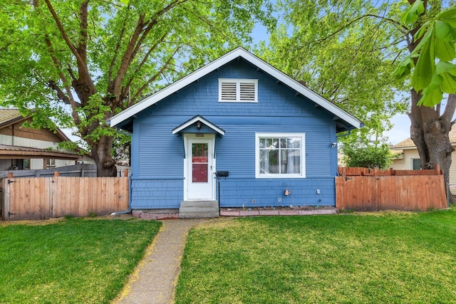 bungalow-style home with fence, entry steps, and a front lawn