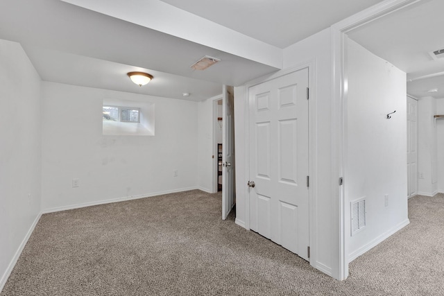 below grade area with baseboards, visible vents, and light carpet