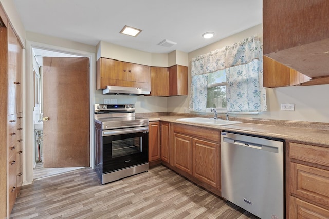 kitchen with a sink, light countertops, under cabinet range hood, stainless steel appliances, and light wood-style flooring