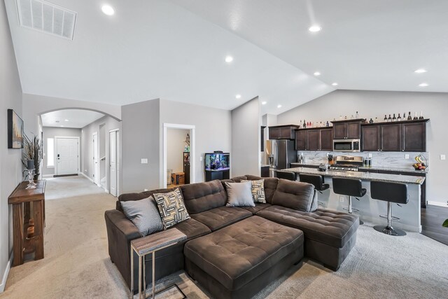living room with visible vents, lofted ceiling, recessed lighting, light colored carpet, and arched walkways
