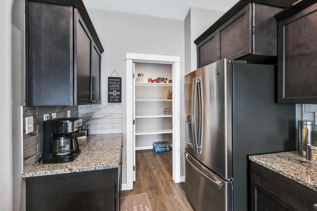 kitchen featuring dark wood-style flooring, dark brown cabinetry, light stone countertops, and stainless steel fridge with ice dispenser
