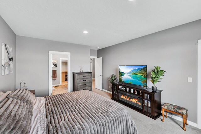 bedroom featuring baseboards, a lit fireplace, recessed lighting, light colored carpet, and connected bathroom