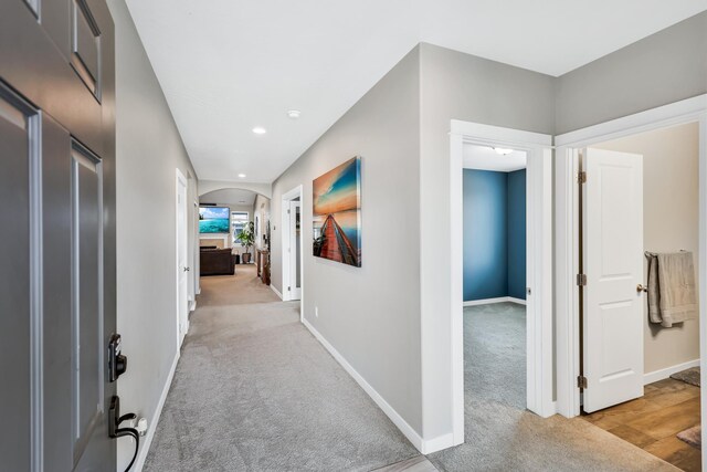 hallway featuring arched walkways, baseboards, light colored carpet, and recessed lighting