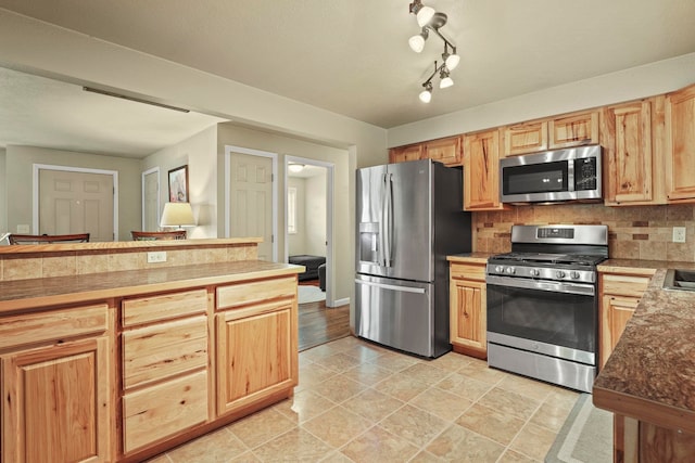 kitchen with baseboards, backsplash, light brown cabinetry, and stainless steel appliances