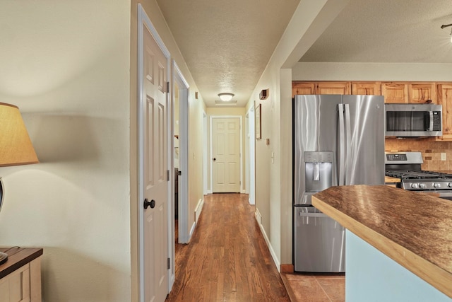 kitchen featuring backsplash, a textured ceiling, dark countertops, appliances with stainless steel finishes, and baseboards