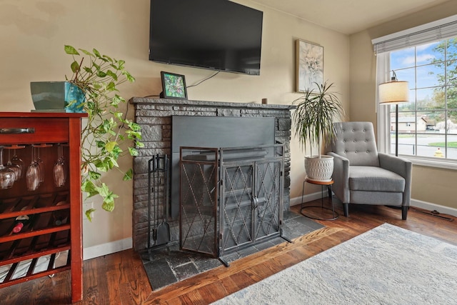 living area featuring baseboards, a fireplace with flush hearth, and wood finished floors