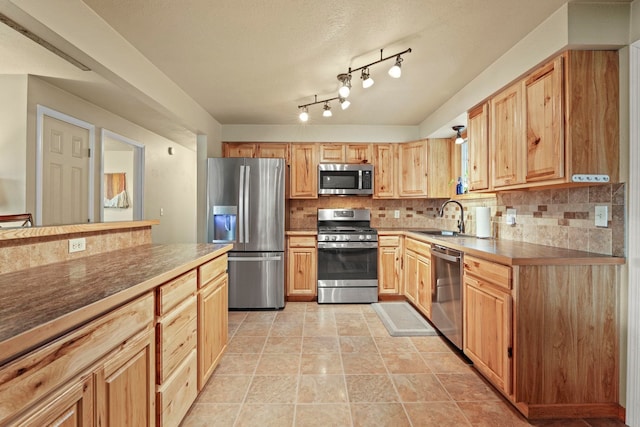 kitchen featuring decorative backsplash, light brown cabinetry, dark countertops, a sink, and appliances with stainless steel finishes