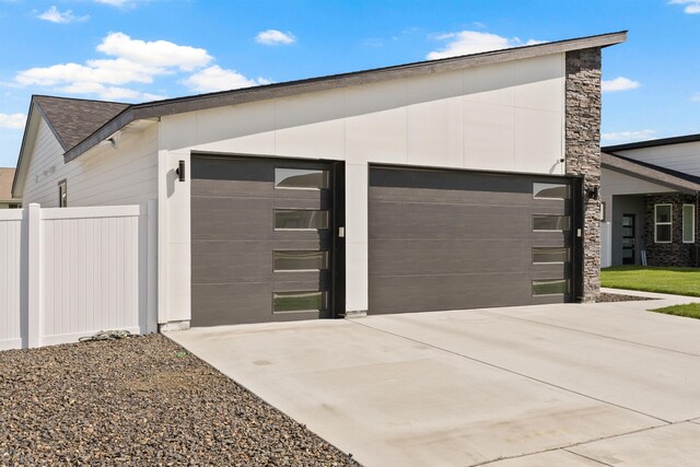 view of home's exterior with fence, stone siding, and a garage