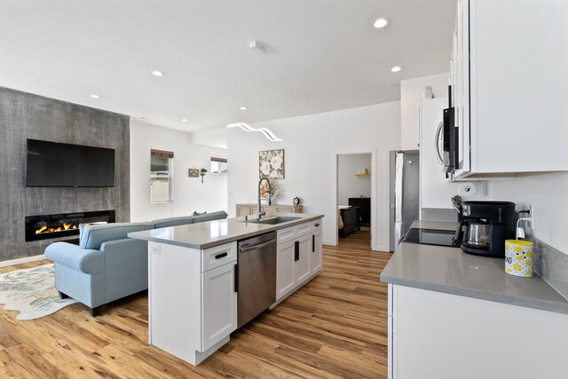kitchen featuring white cabinets, appliances with stainless steel finishes, a sink, light wood finished floors, and open floor plan