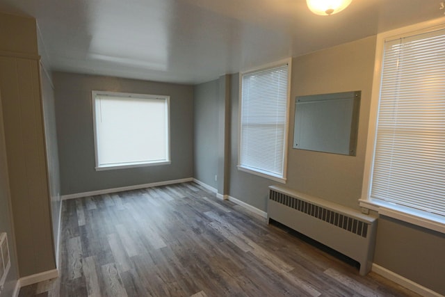spare room featuring baseboards, wood finished floors, and radiator