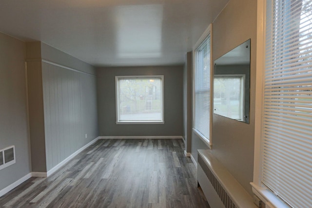 interior space featuring visible vents, wood finished floors, baseboards, radiator heating unit, and a wealth of natural light