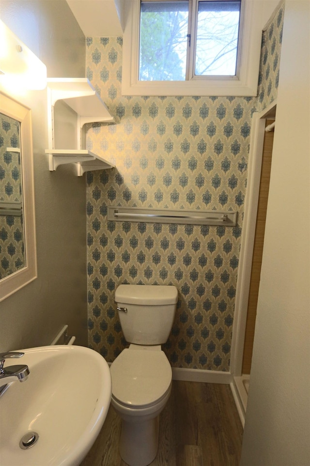 bathroom featuring a sink, toilet, wallpapered walls, a shower stall, and wood finished floors