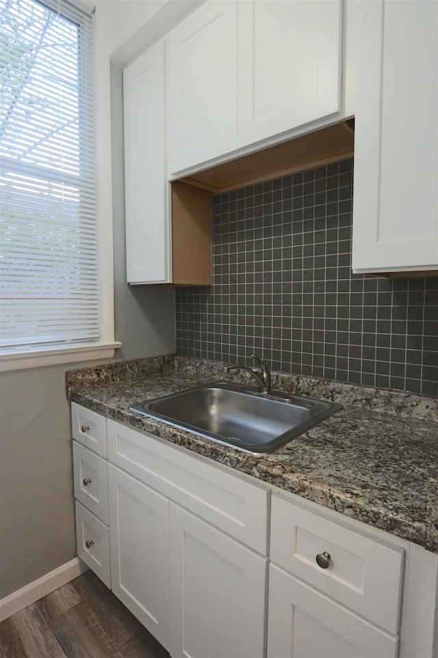 kitchen featuring a sink, baseboards, backsplash, and white cabinetry