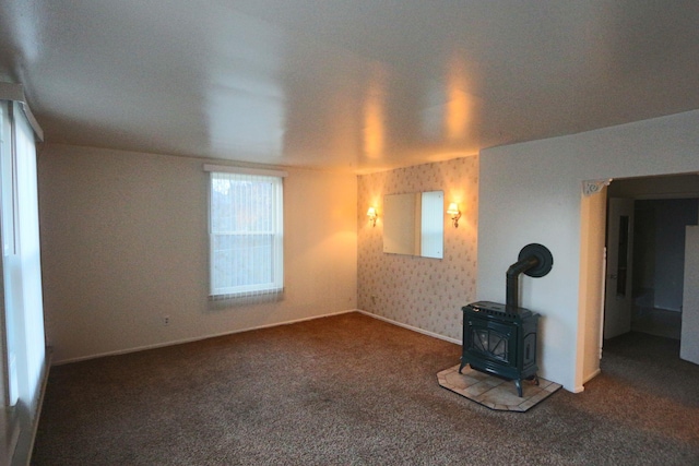 unfurnished living room with carpet floors, baseboards, wallpapered walls, and a wood stove