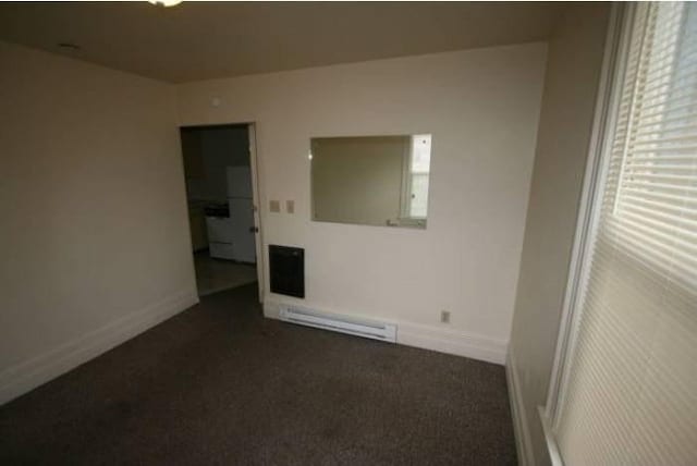 empty room featuring baseboards, baseboard heating, and dark carpet