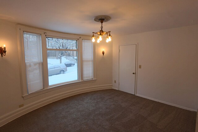 empty room with an inviting chandelier, baseboards, and dark colored carpet