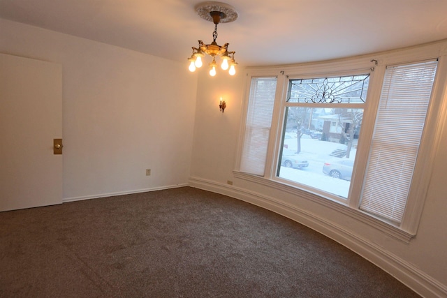 empty room with dark colored carpet, baseboards, and a notable chandelier