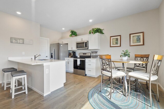 kitchen featuring appliances with stainless steel finishes, a sink, a breakfast bar area, light wood-style flooring, and white cabinetry