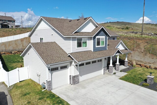 view of front of property with driveway, roof with shingles, a garage, fence, and stone siding