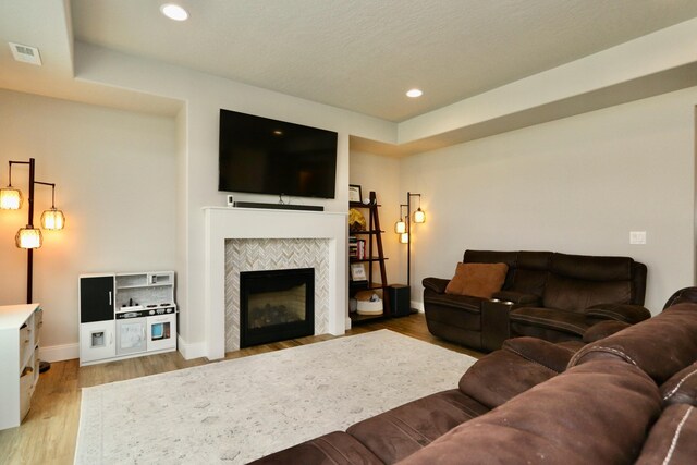 living area featuring baseboards, visible vents, a tiled fireplace, and light wood-style flooring