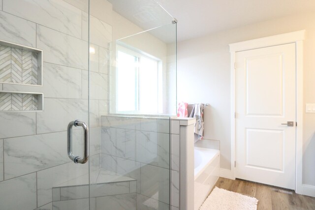 full bathroom with a shower stall, a bath, and wood finished floors