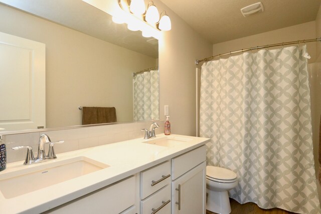 bathroom featuring double vanity, toilet, a sink, and tasteful backsplash