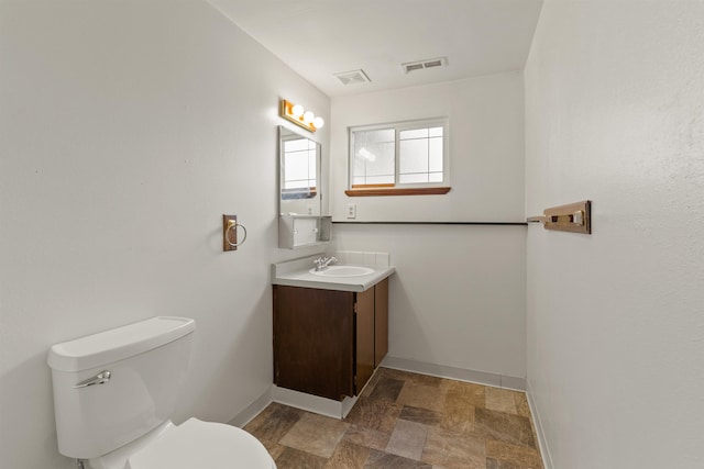 1317 S Woodlawn Rd, Spokane Valley, WA 99216 - half bathroom featuring vanity, toilet, stone finish floor, baseboards, and visible vents