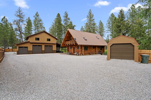view of front facade with a detached garage, fence, an outbuilding, and log exterior