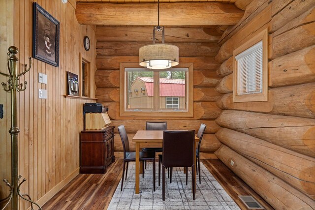dining room with visible vents, log walls, wood finished floors, and beam ceiling