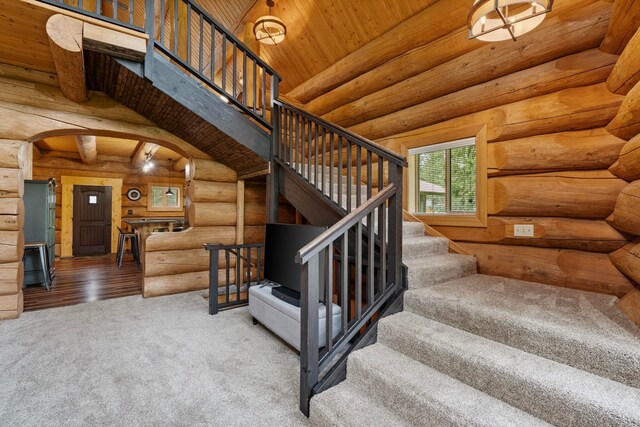 stairway featuring arched walkways, log walls, wooden ceiling, and carpet