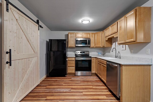 kitchen with light brown cabinetry, a barn door, a sink, light wood finished floors, and stainless steel appliances