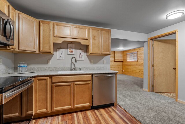 kitchen with wood walls, light brown cabinets, light countertops, a sink, and stainless steel appliances