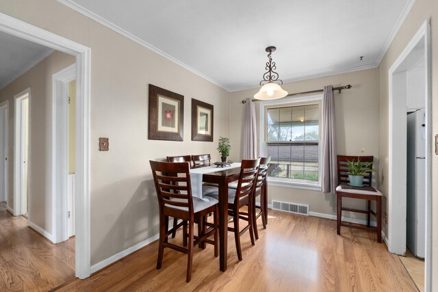 dining area with baseboards, visible vents, ornamental molding, and light wood-style floors